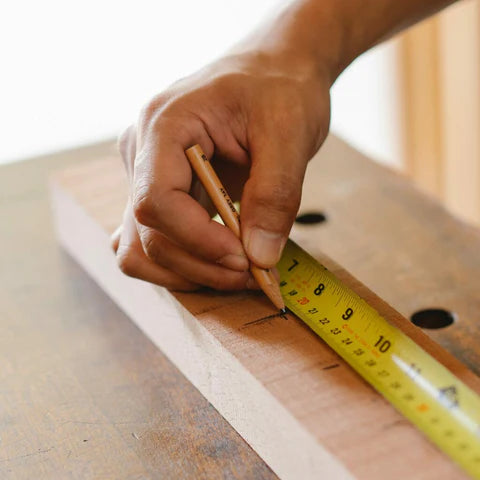 Hand zeichnet Maß auf Holz an.