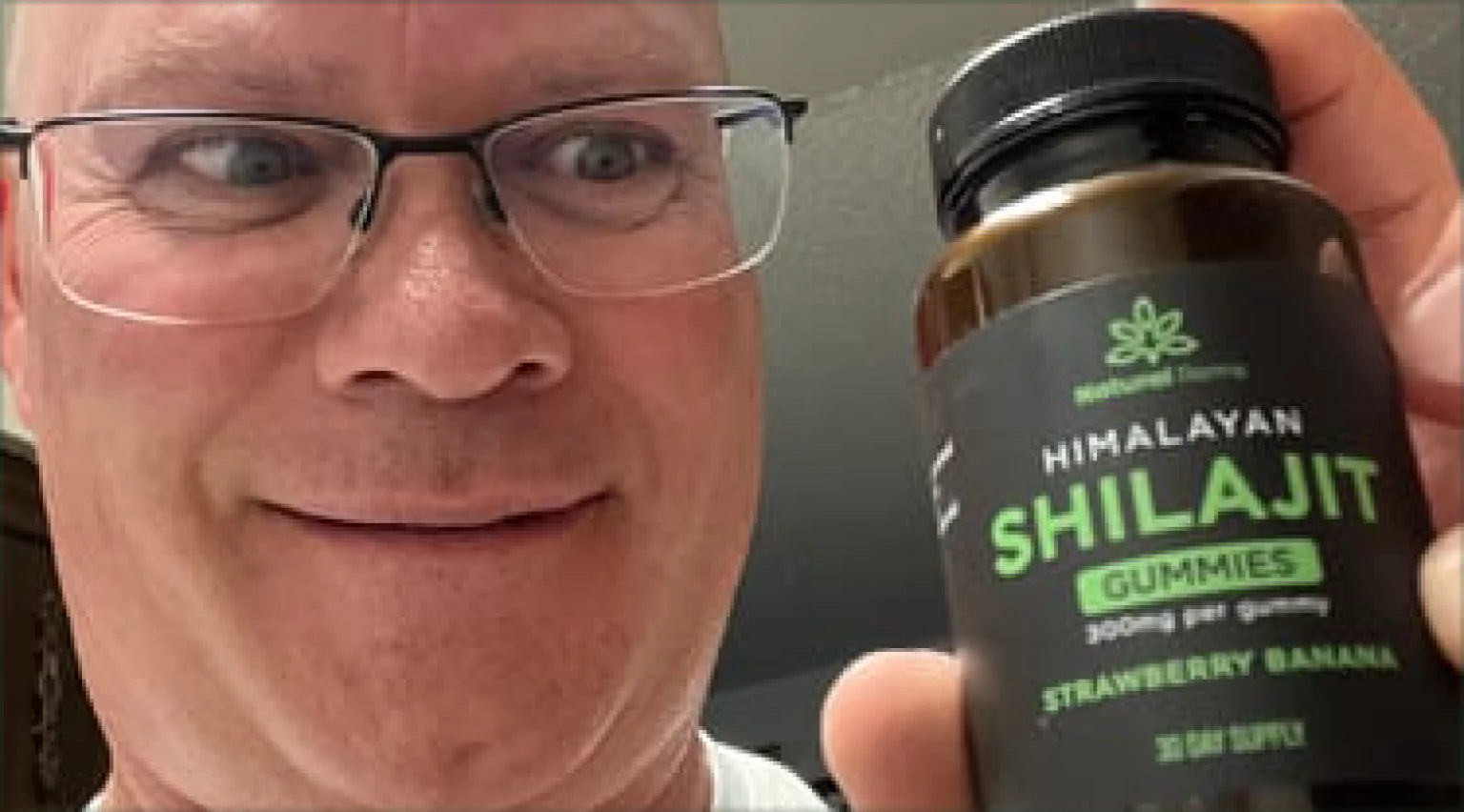 Man holding a bottle of Himalayan Shilajit gummies, strawberry banana flavor.