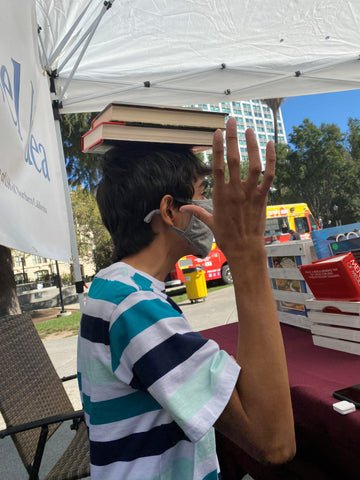 participant Quentin is balancing books on his head while selling books at the market. 