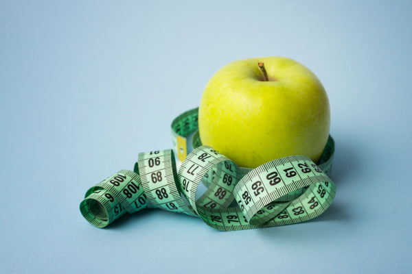 A green apple surrounded by a measuring tape