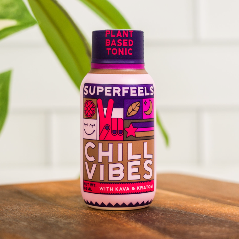 A colorful plant-based tonic bottle labeled 'CHILL VIBES' with icons and text, on a wooden surface.