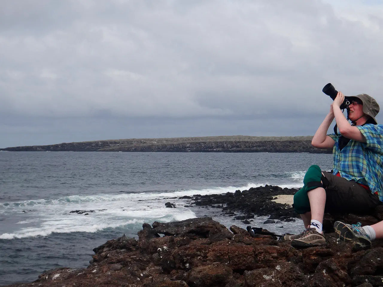 woman photographing bird in sky while sitting on rocks