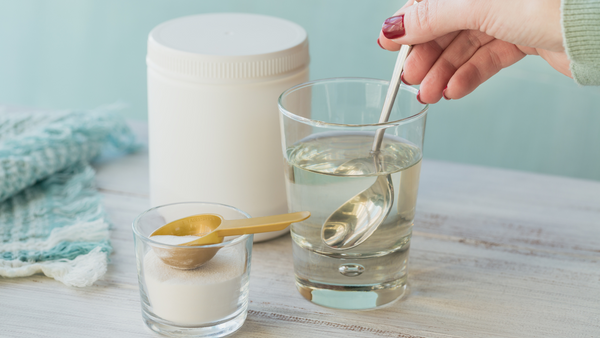 Image depicting a jar of collagen with a hand mixing collagen powder into a glass of water