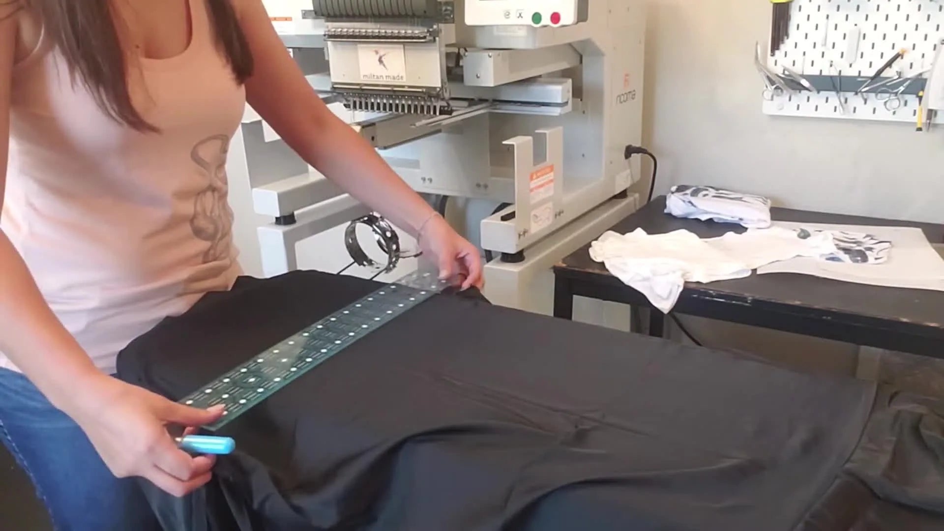Woman marking a horizontal line 3 inches up from the armhole of a black satin robe with a ruler and chalk roller.