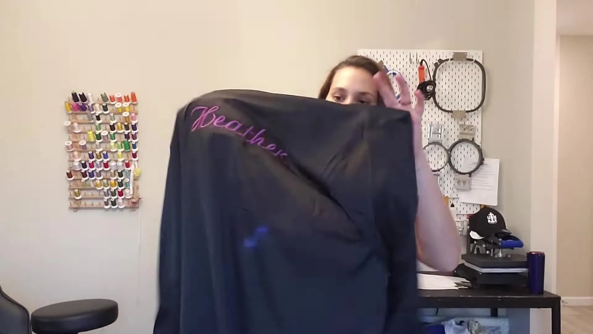 Woman holding up a black satin robe with 'Heather' embroidered in purple on the back.
