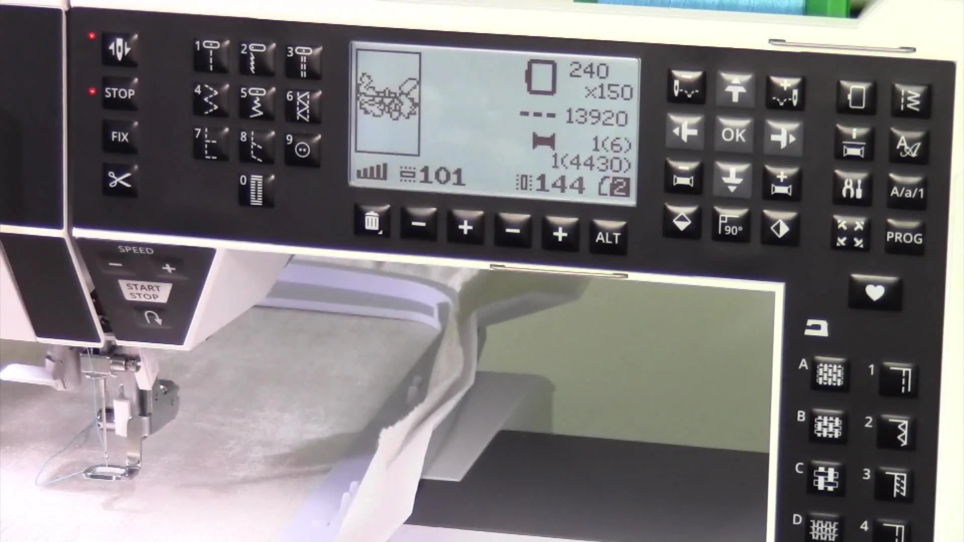 Hand pointing to the embroidery machine's display screen.