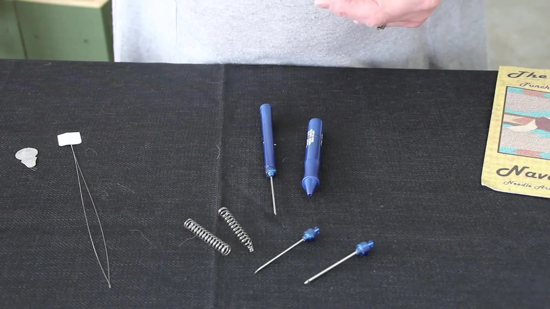 Woman's hands holding blue punch needle handle with separate needle parts