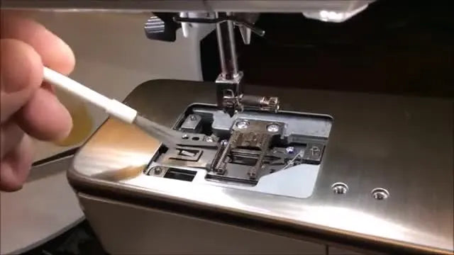 A small white brush gently sweeping lint out of the exposed thread catcher mechanism.