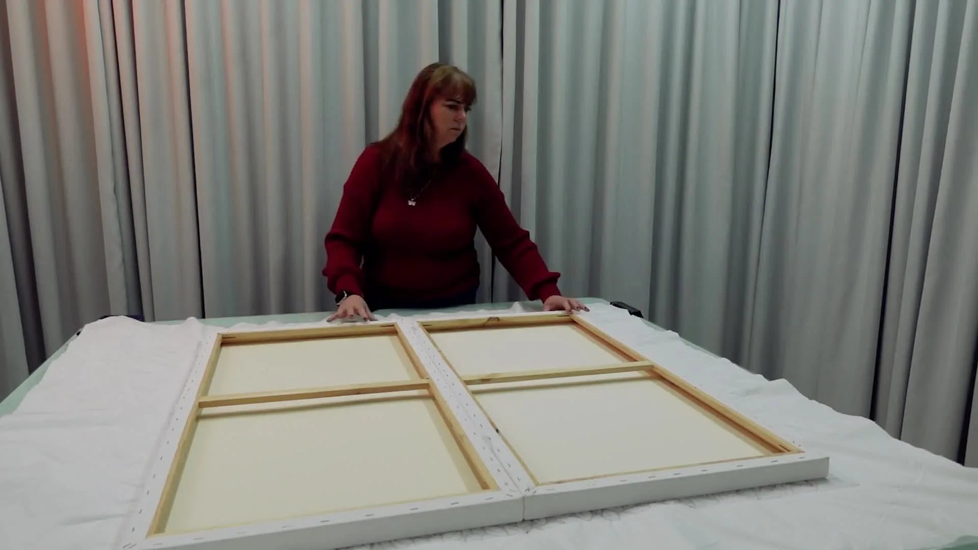 Man using an upholstery staple gun to secure white backing fabric to a canvas frame.