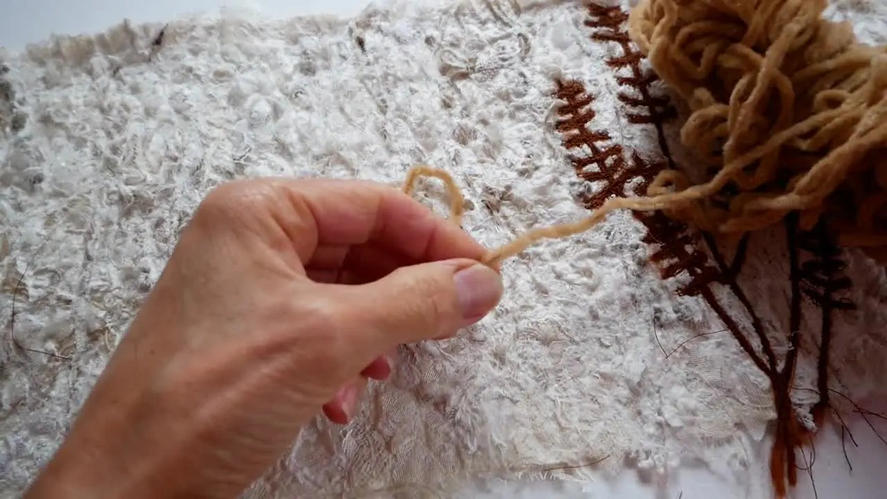 Hands cutting a piece of golden yarn with small scissors.