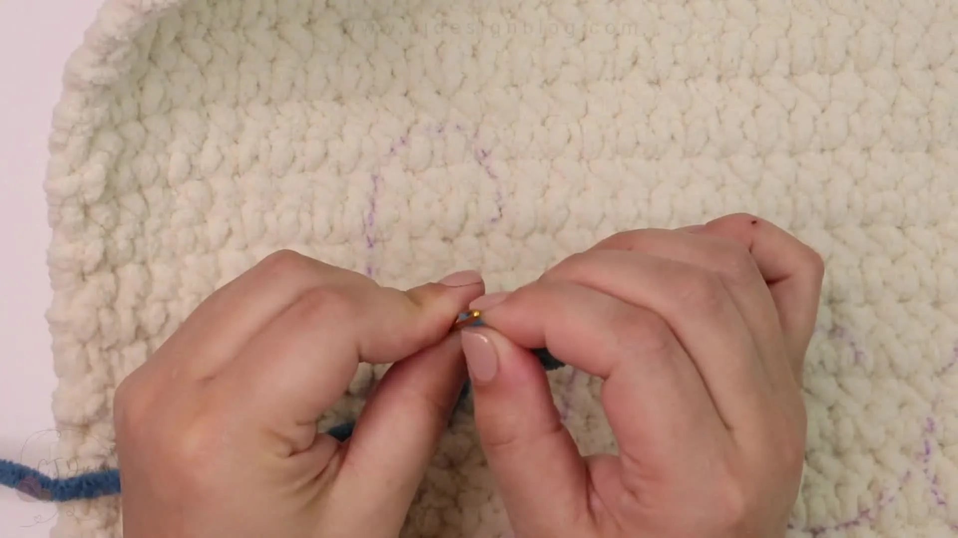 A hand threading a tapestry needle with blue yarn.