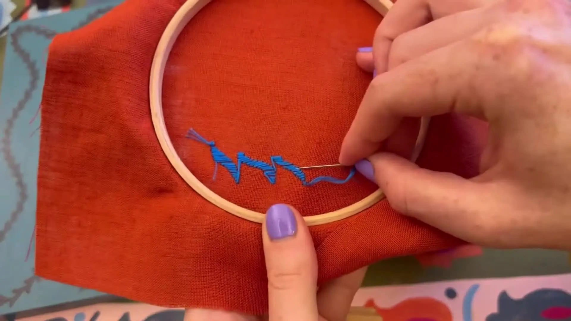 Hands on the back of the embroidery hoop, securing the thread under existing stitches.