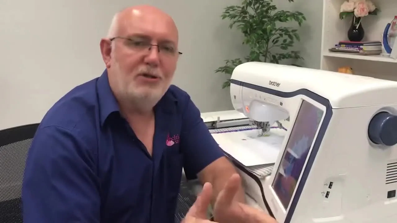 Man in blue shirt, glasses, talking to camera, with embroidery machine in background.