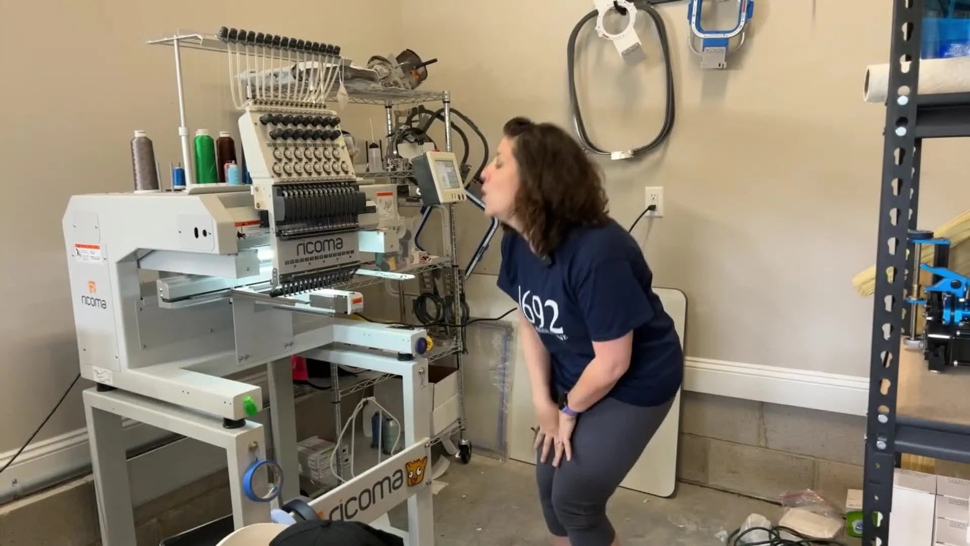 A woman bends down to inspect the needles of her multi-needle embroidery machine.