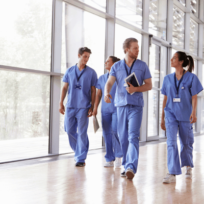The image shows a group of doctors walking. They are wearing blue work clothing and standing indoors. The group consists of men wearing uniforms and trousers.