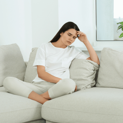 The image shows a woman sitting on a couch, looking like she have headache
