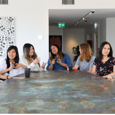 The photo is of a group of women sitting at a table indoors. They are smiling and seem to be having a good time.