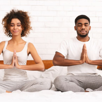 The image shows a man and a woman sitting on the floor indoors. Both individuals are smiling. The man is wearing a t-shirt.