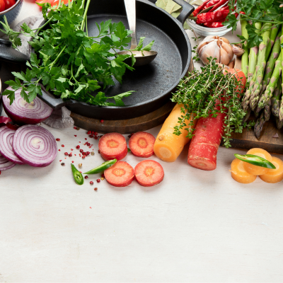 The image shows a variety of vegetables displayed on a table, including carrots, radishes, parsley, and onions. It represents a selection of natural, vegan-friendly produce and ingredients for cooking.