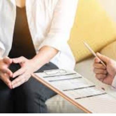 The image is of a person drawing on a piece of paper using office supplies in an indoor setting. The woman sitting seems to be in a meeting with a doctor.