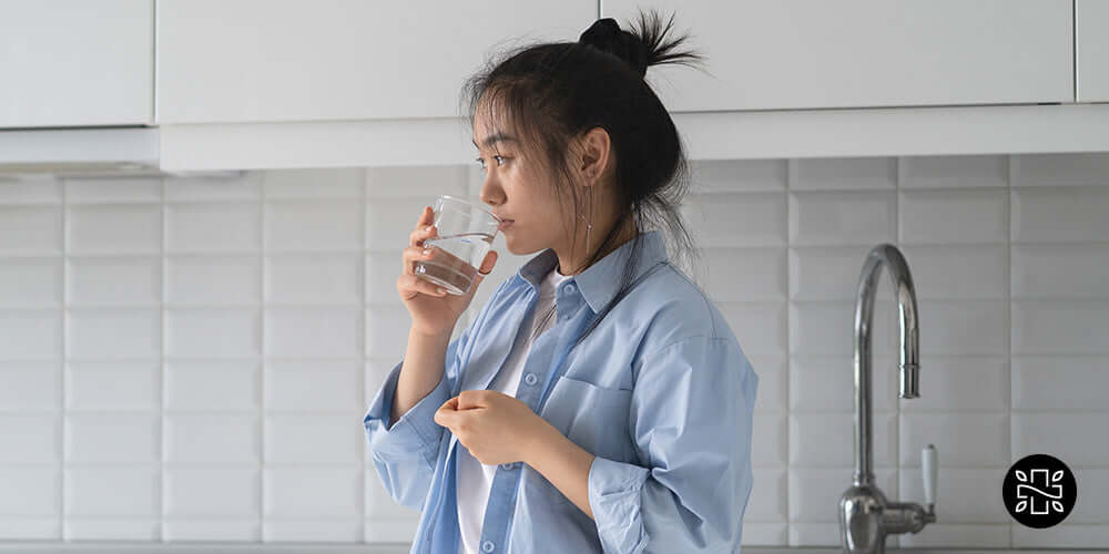 Mujer asiática pensativa tomando medicamentos con un vaso de agua en la mano