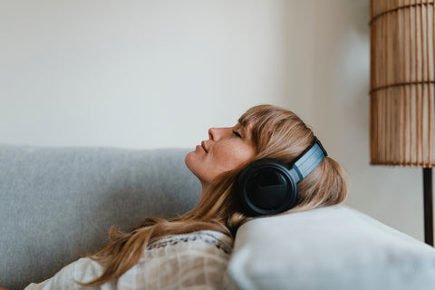A woman lay with her eyes closed on a sofa wearing headphones.