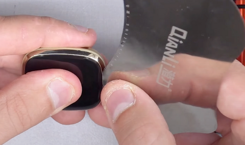 Inserting your thin pry tool and pushing it around the edge of the Fitbit Sense screen