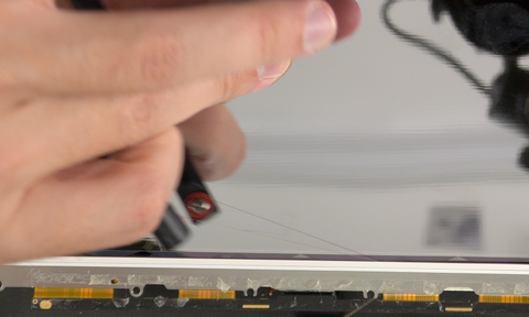Sliding a wire back and forth behind a metal bracket on the A2338 MacBook to remove it from the old screen
