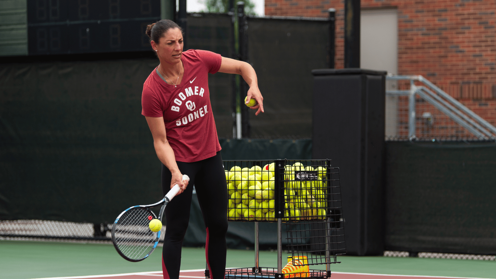 Audra Coach feeds tennis balls from a big basket on court.