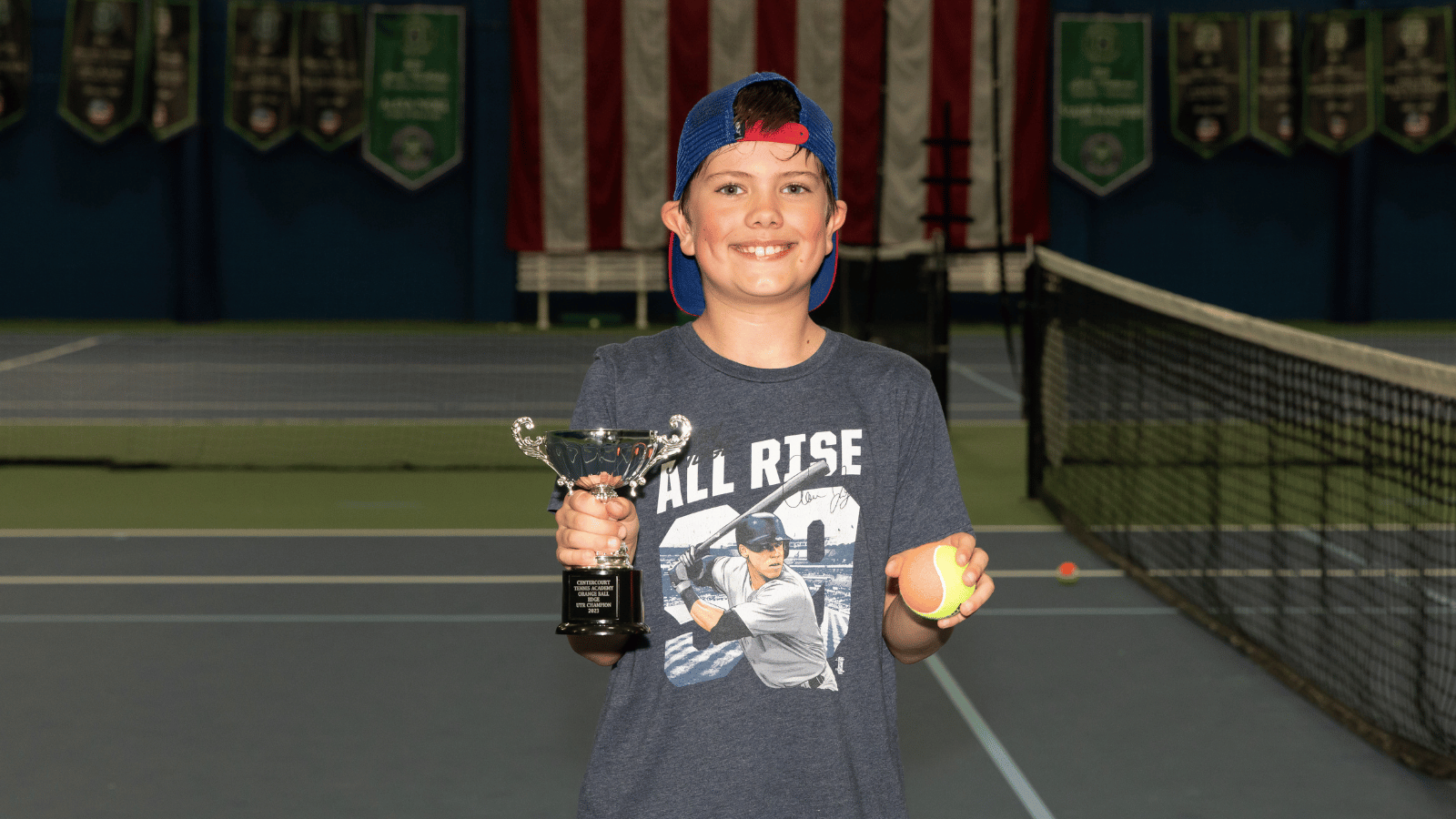Young boy poses with trophy and orange ball after winning tournament