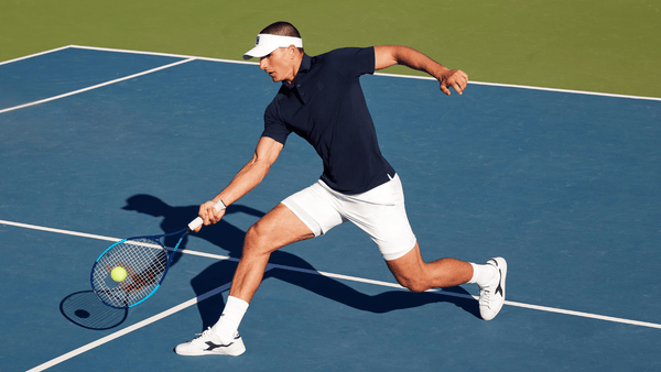 A man hits a tennis ball on a court wearing Fabletics clothing.
