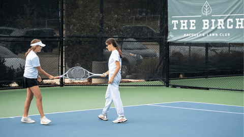 Two young girls tap racquets at The Birch tennis club in Texas.