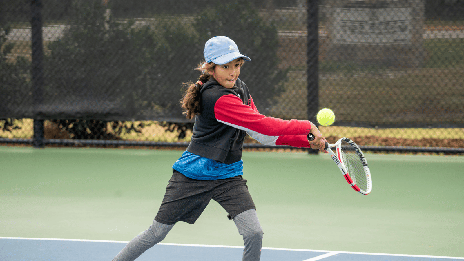 A young girl hits a backhand on a tennis court.