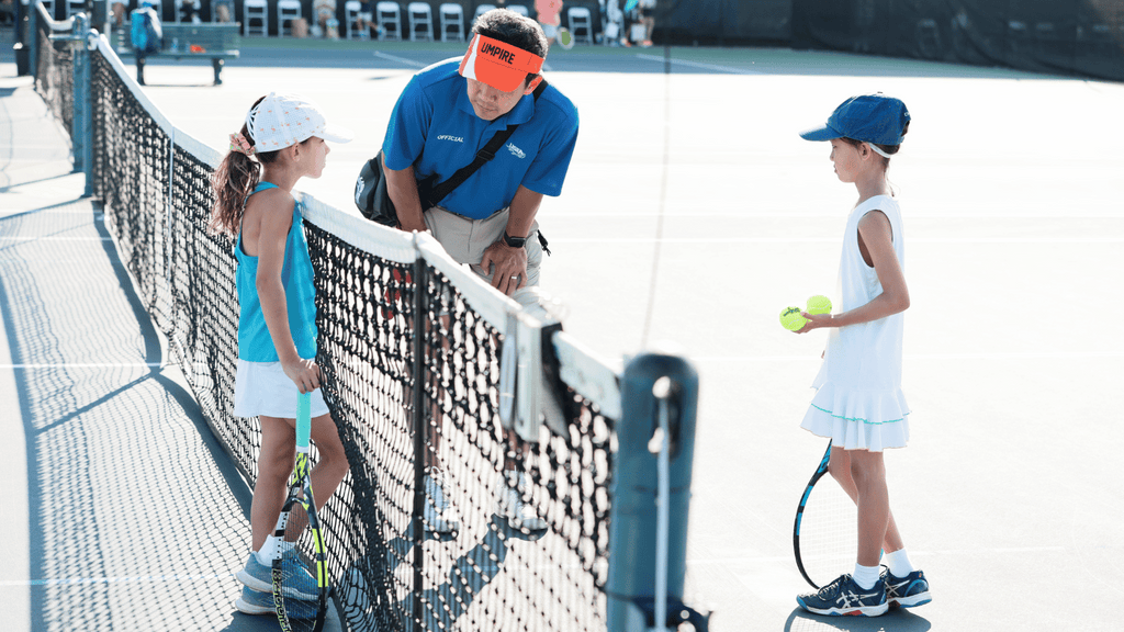 Two young girls at the net with an umpire at a Little Mo tournament.