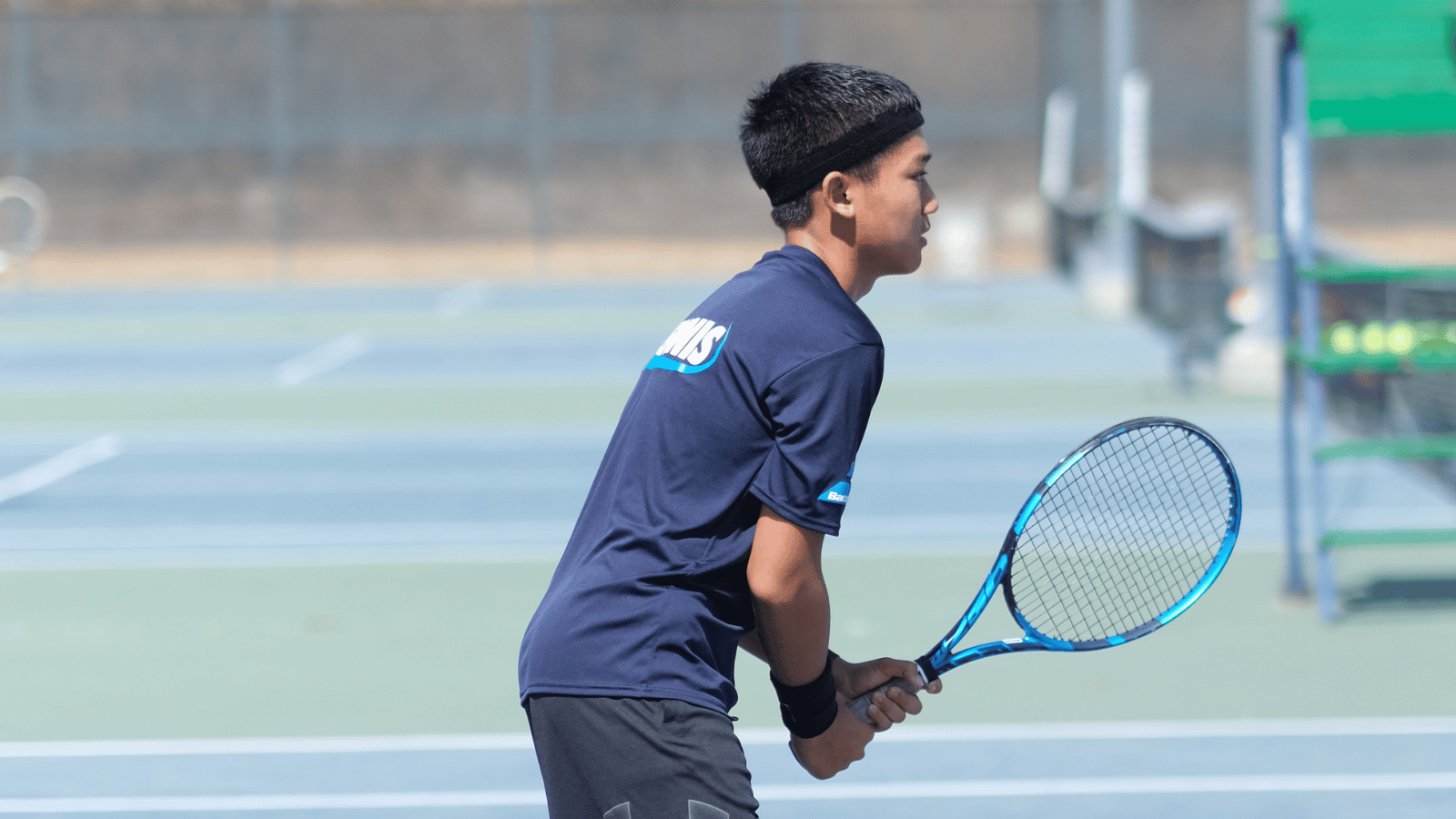 Boy in ready position on court holding racquet.