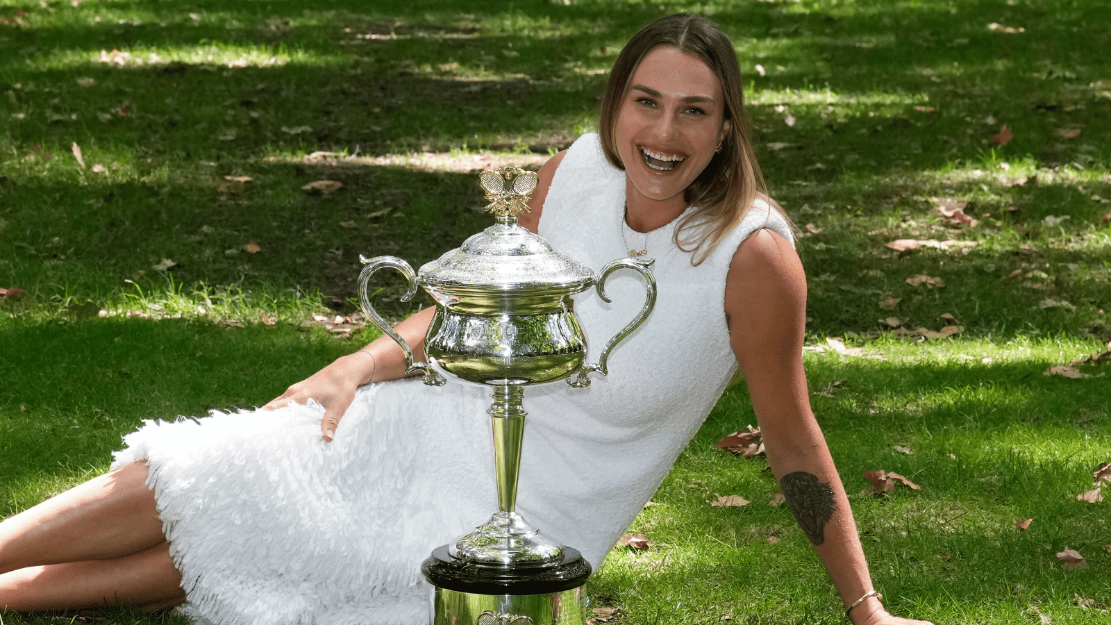 Aryna Sabalenka poses in the grass with the 2024 Australian Open trophy.