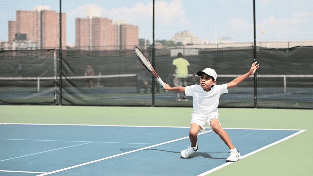 A young boy hits a one-handed slice on a tennis court.