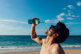 homme sur la plage qui boit de l'eau de bouteille en verre