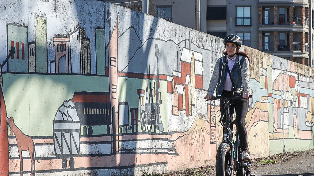 Woman riding Emerald Ebike down the street in front of a mural