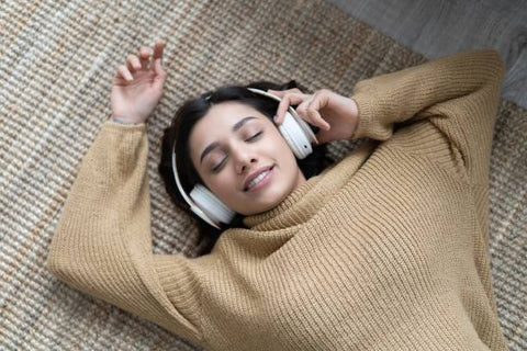 A woman lays on the floor listening to music through headphones.