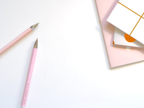  An image of two pink ballpoint pens and other stationery supplies.