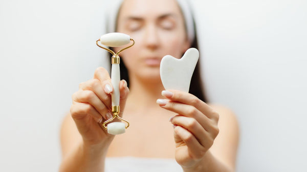 A woman at a spa holding white gua sha tool and a facial roller