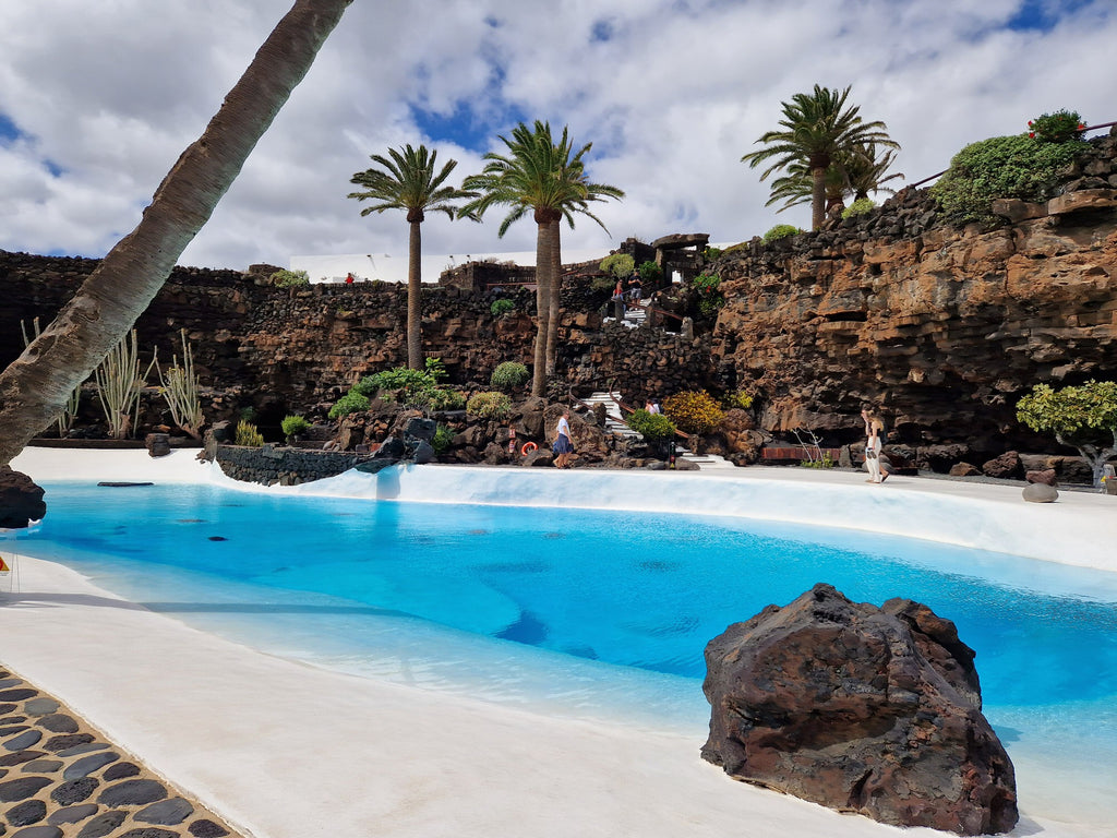 Bright blue of the artificial lake surrounded by palm trees and volcanic rock.