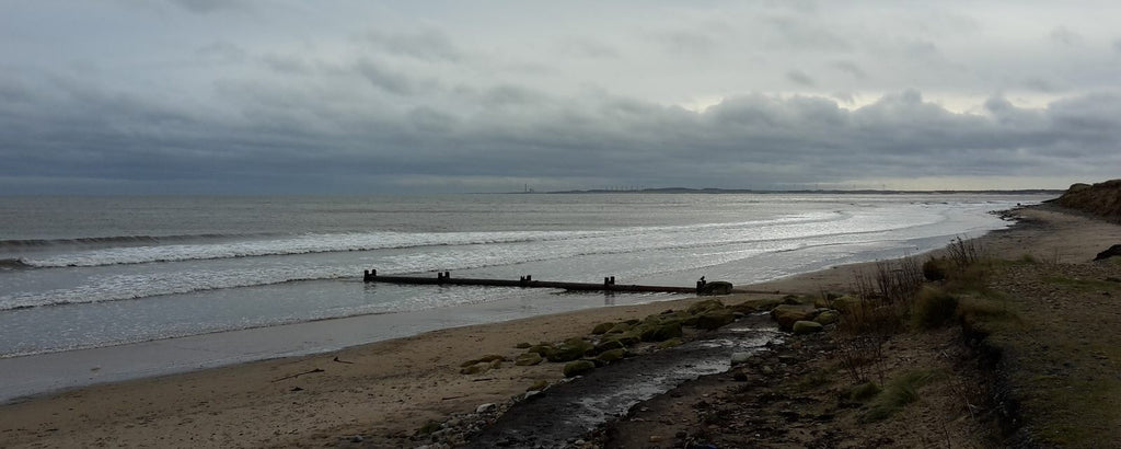 Grey stormy skies with waves rolling into a sandy beach with groyne.