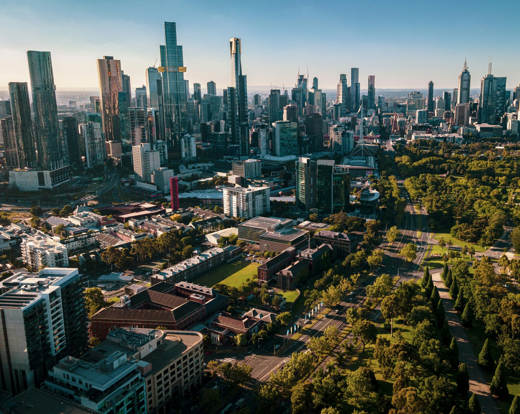 Aerial view of Melbourne city skyline with towering skyscrapers and green parkland.