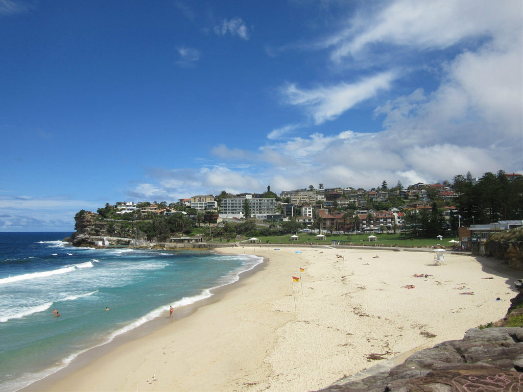 Looking down at soft sandy beach with grassy park and buildings set into the cliffs in the distance