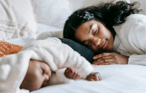 New mother enjoying a serene moment of rest alongside her sleeping baby, emphasizing the importance of comfort and relaxation in the postpartum journey.