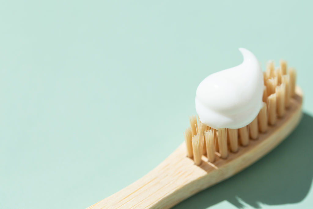 White toothpaste on natural bamboo toothbrush with aqua background