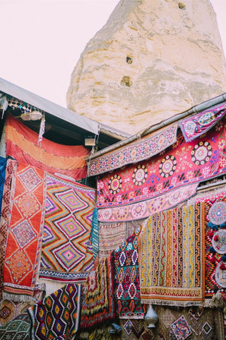 A variety of colourful hand-woven rugs displayed outside a shop on a market