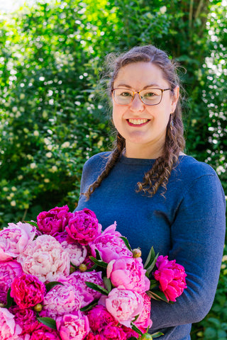 Lorelie smiling at the camera while holding a large bunch of mixed pink peonies